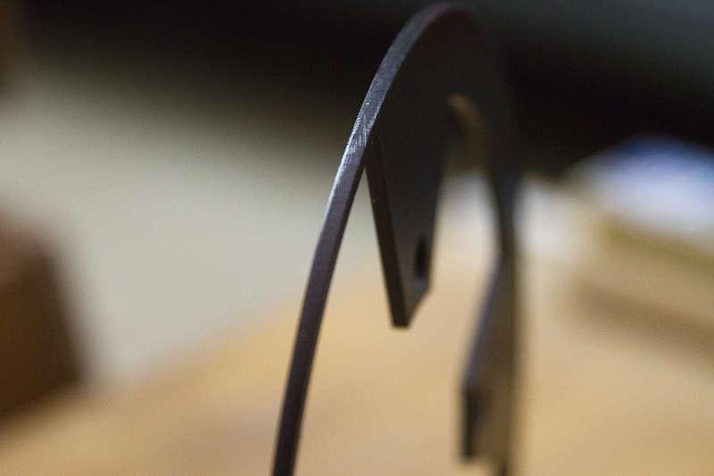 BBG Bashguard: A close-up image of a sleek, curved metallic sculpture, highlighting its smooth surface and sharp angles. The object is partially blurred in the background, creating a soft focus effect, with warm wooden textures visible beneath it.