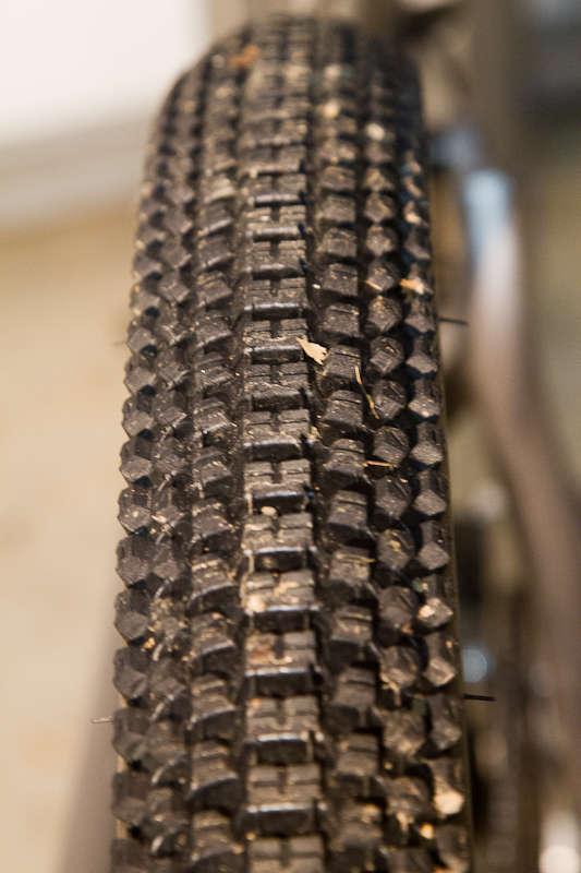 Kenda Small Block Eight: Close-up image of a textured bicycle tire showing the tread pattern and some debris. The background is out of focus, highlighting the tire's details.