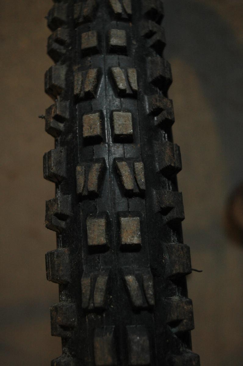 Maxxis Minion DHF: Close-up view of a worn mountain bike tire with distinct tread patterns, showing dirt and debris embedded in the rubber.