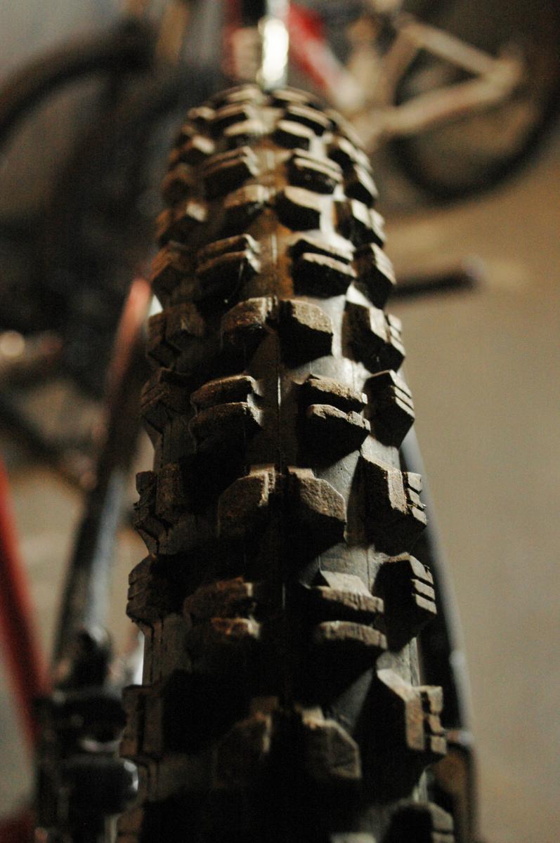 Maxxis Minion DHR: Close-up view of a mountain bike tire, showcasing the textured tread pattern designed for traction on various terrains. The background is slightly blurred, highlighting the tire while other bike elements are faintly visible.