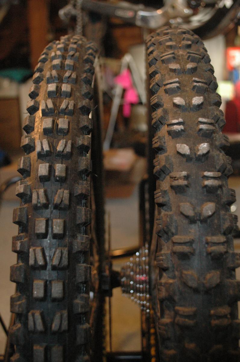 Maxxis Minion DHR: Close-up view of two mountain bike tires with pronounced tread patterns, showcasing dirt and wear. The background is slightly blurred, suggesting a garage setting.