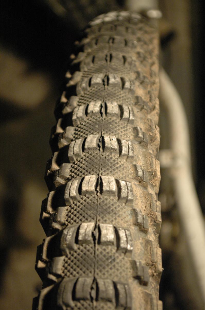 WTB Prowler MX: Close-up of a muddy mountain bike tire, showing the tread pattern and wear on the rubber. The background is blurred, emphasizing the texture and details of the tire.