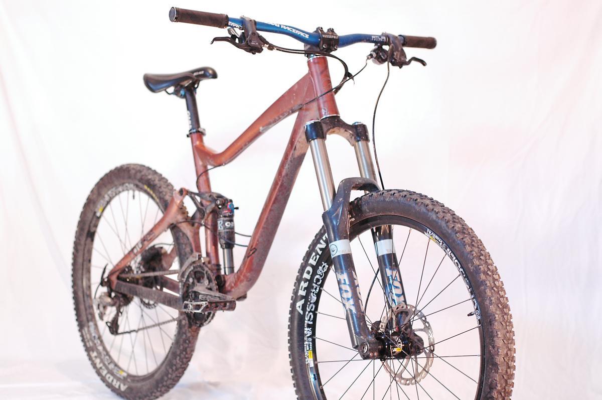 Giant Reign 1: A mountain bike with a maroon frame, equipped with front suspension forks, wide tires, and disc brakes, positioned against a plain white background. The bike shows signs of use with dirt on the tires and frame.