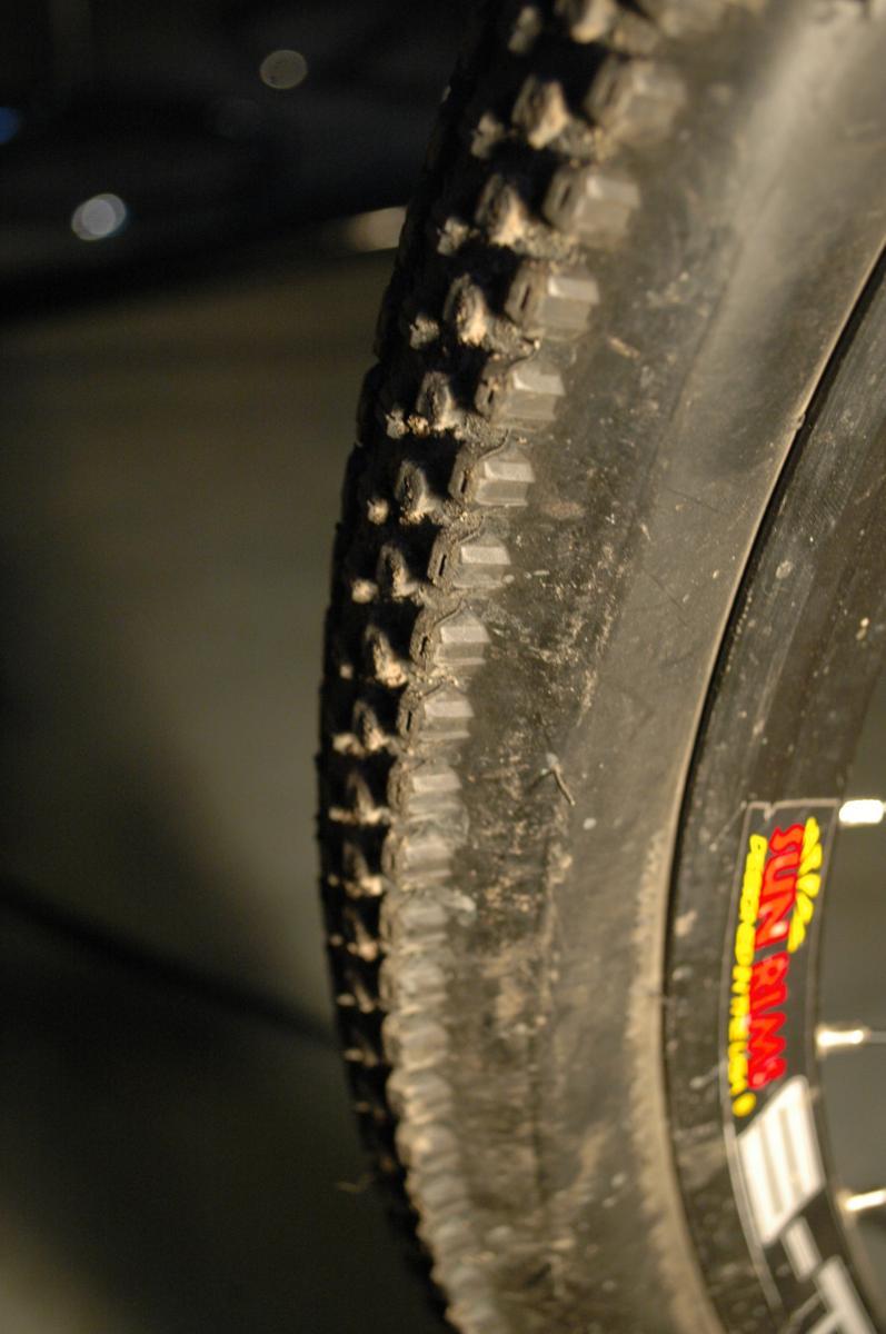 Kenda Small Block Eight: Close-up of a bicycle tire showing the tread pattern and sidewall details. The tire is slightly dirty, indicating use, and a logo on the sidewall reads "Sun Rims."