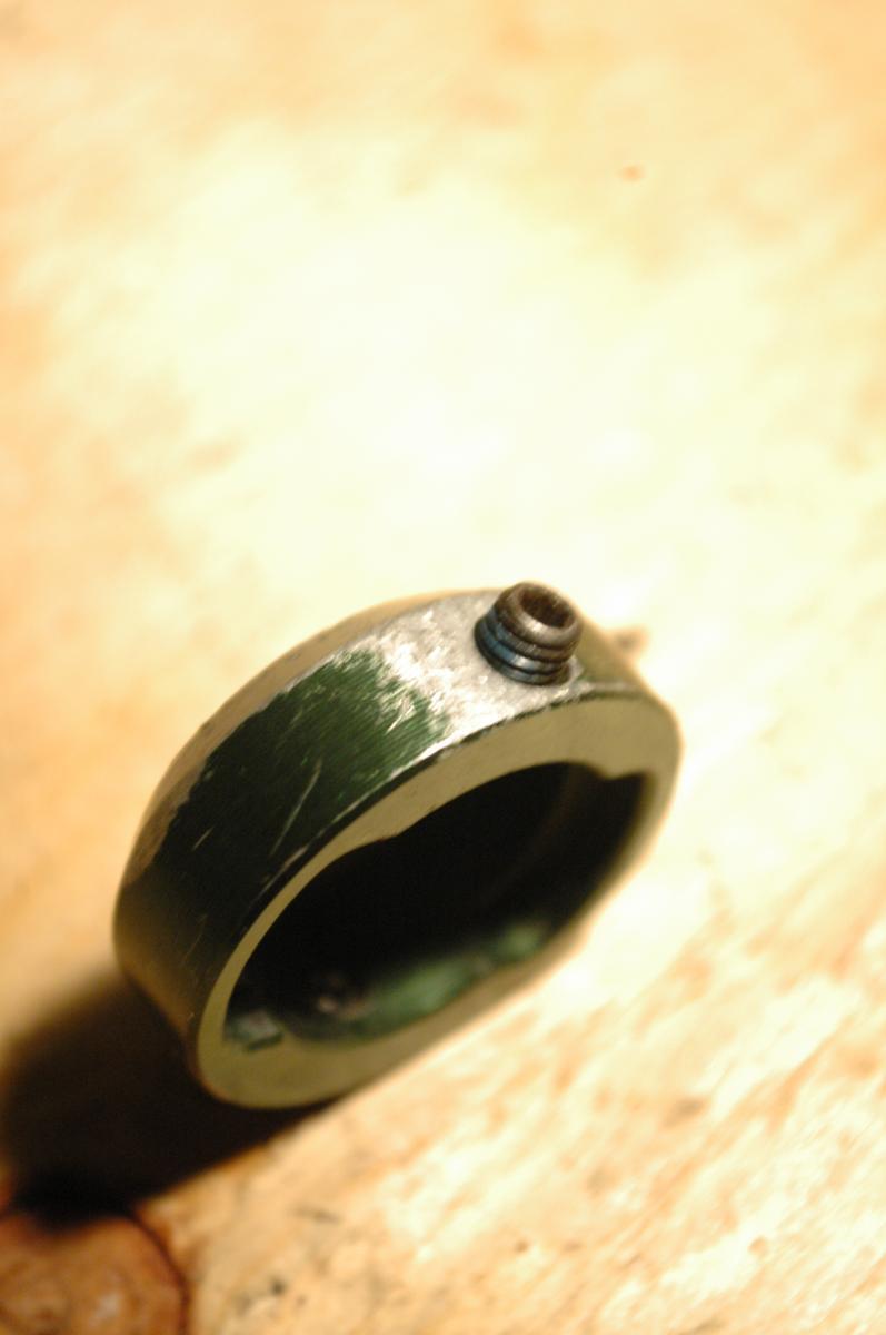 Transition Bar End Caps: Close-up image of a worn green metal ring with a protruding bolt. The ring has visible scratches and a rough surface, placed on a wooden surface with a soft, blurred background.