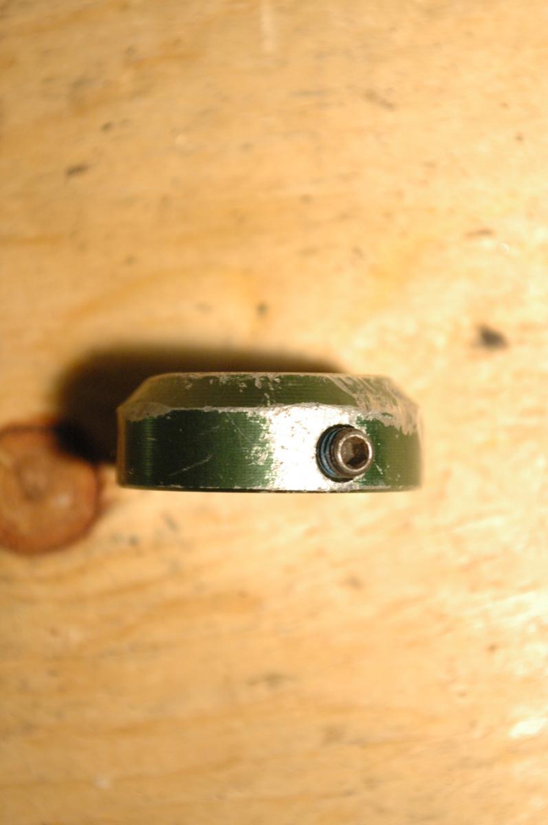Transition Bar End Caps: A close-up view of a green, circular metal object with a slightly worn surface and a small screw on the edge, placed on a wooden surface.