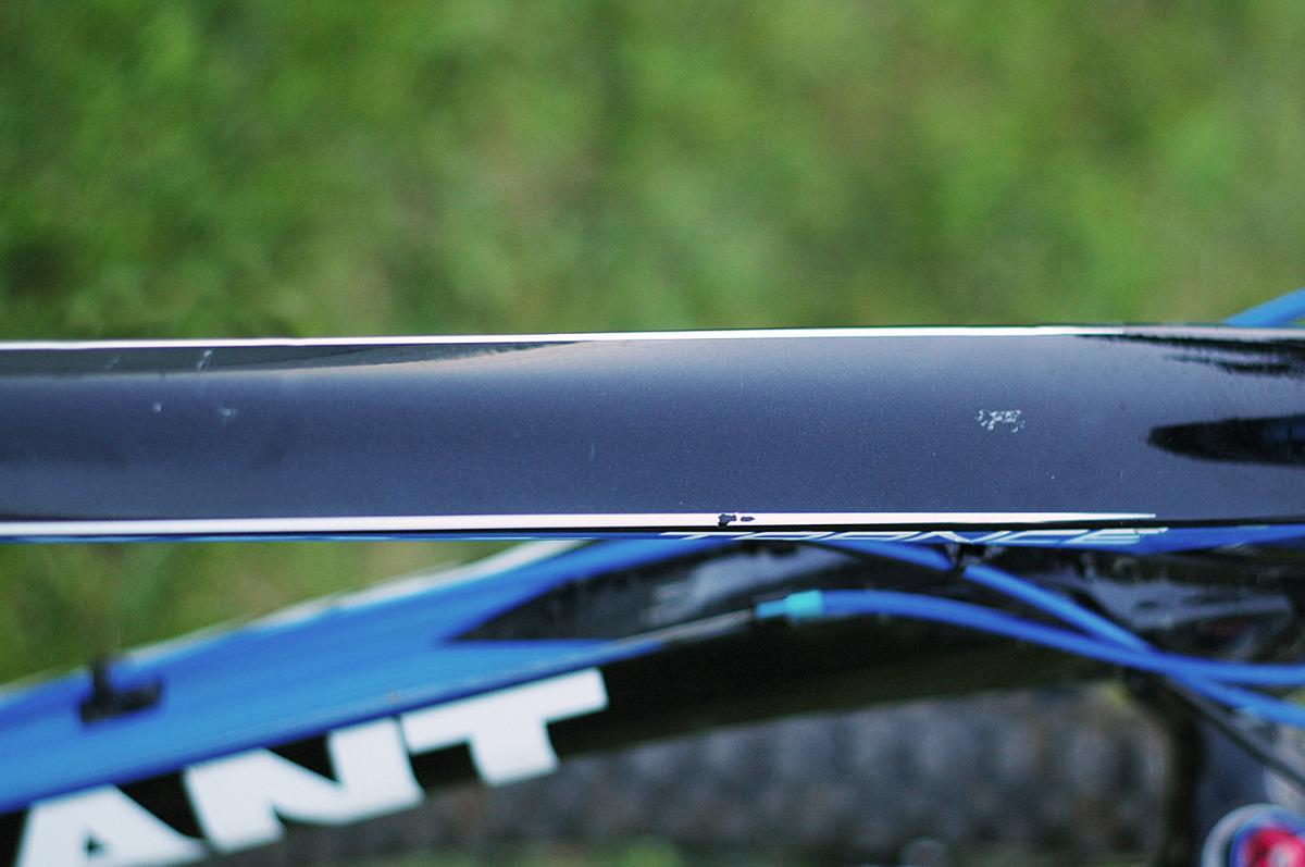 Giant Trance X2: Close-up of a bicycle frame showing a black top tube with minor scratches and a sleek design, set against a blurred green background.