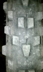 WTB Moto Raptor: Close-up image of a dirt bike tire tread showing distinct patterns and textures, indicative of off-road use. The tire appears worn and is covered in dirt, emphasizing its use on rugged terrain.