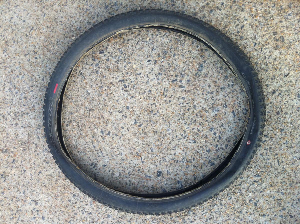 Specialized Fast Trak LK Pro: A black bicycle tire lying flat on a concrete surface, showing signs of wear and lack of air, with a visible red mark on the sidewall.