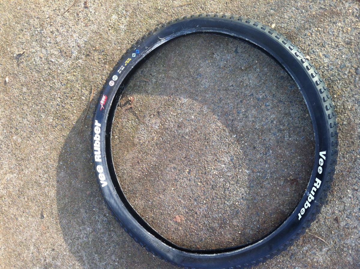 Vee Rubber V8: A bicycle tire resting on a textured surface, featuring the brand name "Vee Rubber" printed in white along the side. The tire shows visible tread patterns and has a circular shape, with no inner tube present.