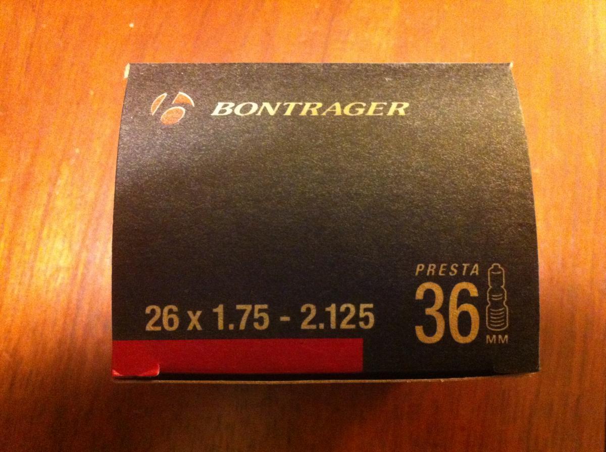 Bontrager Premium Tube: Box packaging for a Bontrager Presta valve bicycle tube, labeled for sizes 26 x 1.75 to 2.125 and featuring a 36 mm valve. The background is black with gold and red text.