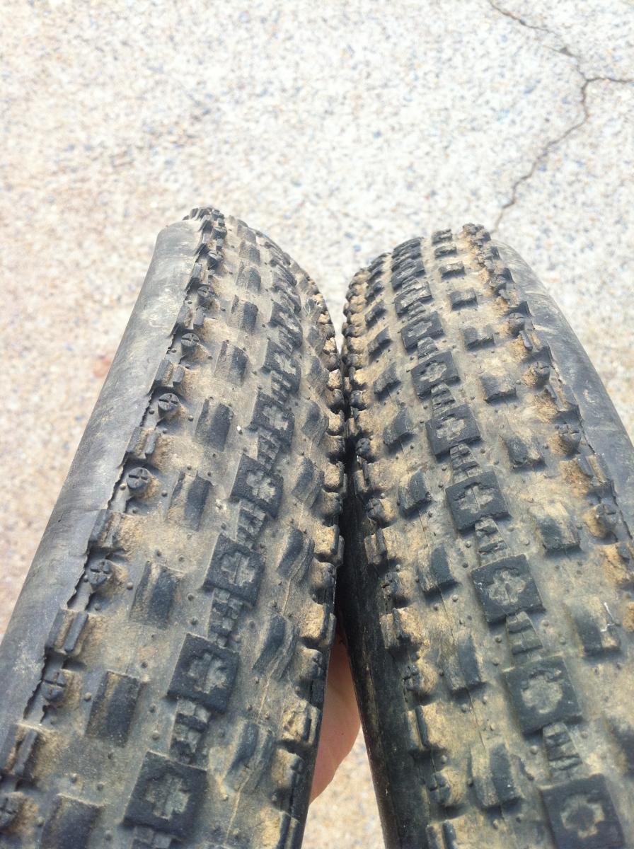 Maxxis Crossmark UST: Alt text: Close-up view of two bicycle tires held side by side, showing different tread patterns and levels of wear. The left tire appears more worn with smoother surface, while the right tire has deeper treads and looks newer. The background is a textured, light-colored gravel surface.
