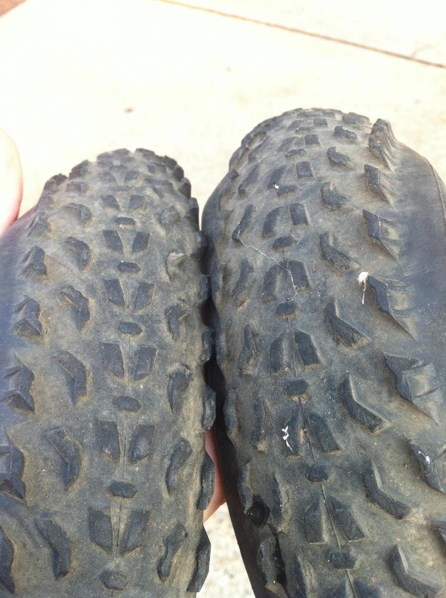 Specialized Fast Trak LK Pro: Two bicycle tires are held side by side, showing their tread patterns. The tire on the left appears to be more worn, while the tire on the right is in better condition. The background is a blurred concrete surface.