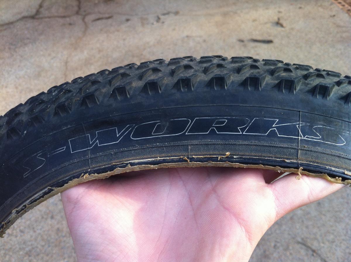 Specialized Fast Trak LK Control: A hand holding a worn mountain bike tire with a textured tread pattern, featuring the brand name "S-WORKS" etched on the sidewall.
