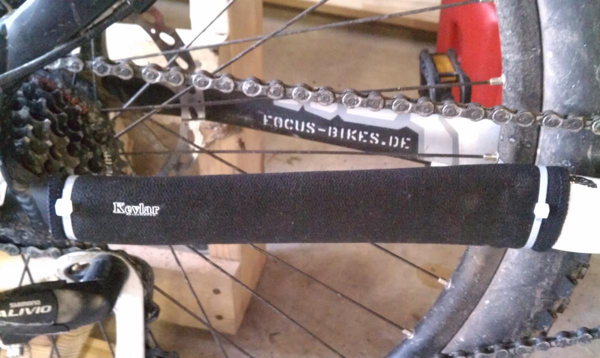 Sette Kevlar/Neoprene Chain Stay Protector: Alt text: Close-up of a bicycle chain with a protective Kevlar sleeve covering part of the chainstay, and visible components including the rear derailleur and cassette. The bike frame has the "Focus-Bikes.de" logo.