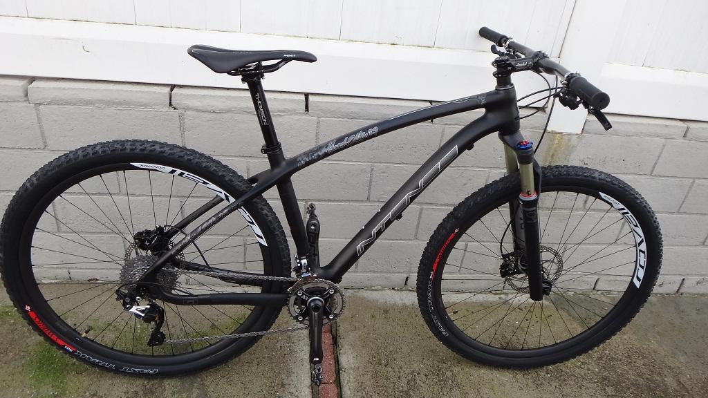 Specialized S-Works Stumpjumper FSR Carbon: A sleek black mountain bike with wide tires and a lightweight frame, positioned against a gray brick wall. The bike features a front suspension fork, disc brakes, and modern handlebars, showcasing its readiness for off-road cycling adventures.