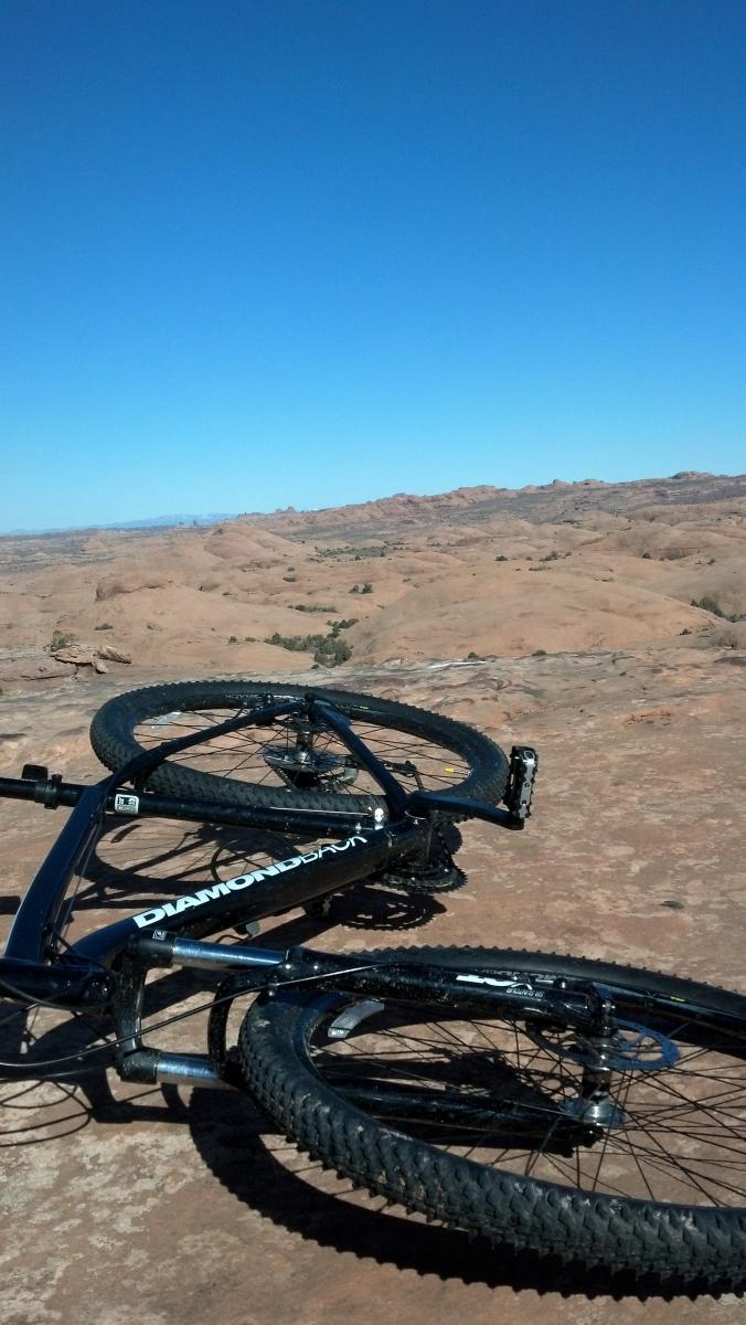 Diamondback Overdrive: A mountain bike lying on its side on rocky terrain, with a clear blue sky in the background and expansive desert hills stretching into the distance.
