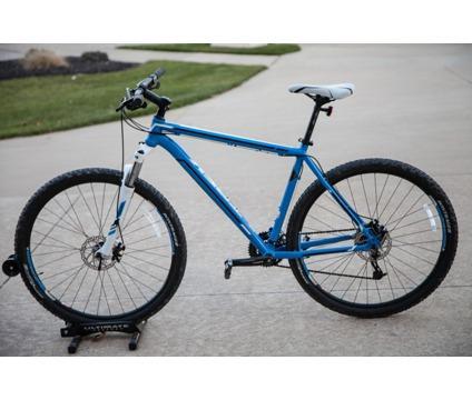Trek Marlin: A blue mountain bike with thick tires, positioned on a concrete surface. The bike features front suspension, a single rear gear, and a streamlined frame design. A grassy area is visible in the background.