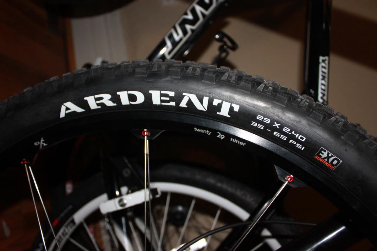 Scott Spark 29 Elite: A close-up image of a mountain bike tire featuring the brand name "Ardent." The tire is labeled with specifications that read "29 x 2.40" and a pressure range of "35-65 PSI." The background includes parts of a bike frame and spokes.