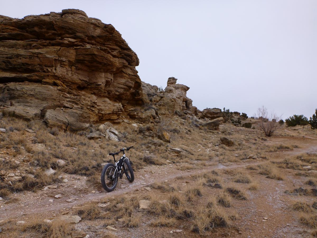 A mountain bike is parked on a dirt path surrounded by rugged rock formations and sparse vegetation, under a cloudy sky. White Ridge Bike Trails mountain bike trail.