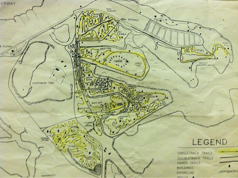 Map showing a layout of trails and facilities, with annotated areas for singletrack, doubletrack, and paved trails, as well as landmarks such as cabins, a shoreline, and an equipment yard. The map is sketched with black lines and highlighted in yellow for better visibility. Oleta River State Park mountain bike trail.