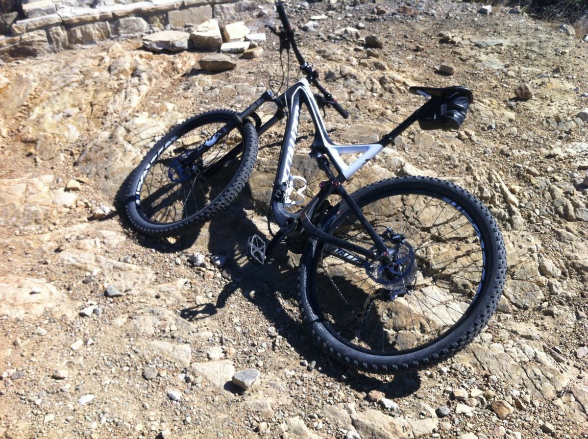 Specialized Stumpjumper FSR: A mountain bike lying on rocky terrain, surrounded by gravel and small stones. The bike features a black and white frame and thick tires designed for off-road riding.