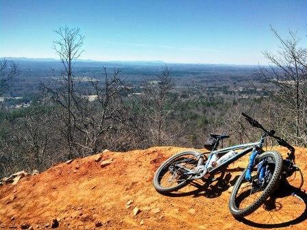 A mountain bike resting on a rocky outcrop overlooking a vast landscape of trees and rolling hills under a clear blue sky. Coldwater Mountain mountain bike trail.