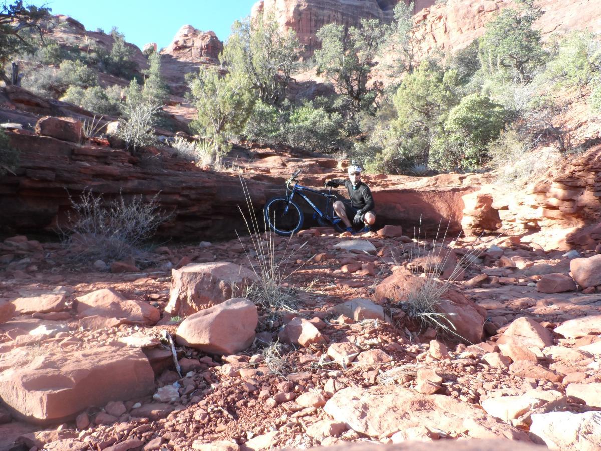 Giant Revel 2: A person sitting beside a mountain bike on a rocky trail surrounded by red rock formations and sparse vegetation under a clear blue sky.