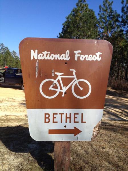 Sign for a National Forest with a bicycle icon and an arrow pointing right towards Bethel. The sign has a brown background with white lettering and symbols. Bethel Bike Trails mountain bike trail.