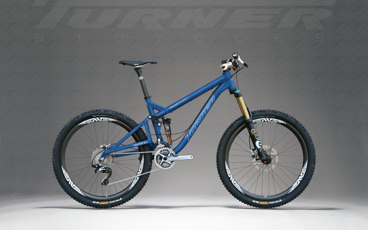 Turner 5.Spot: Alt tag: A blue Turner mountain bike displayed against a gray background, showcasing its sleek design and components, including the frame, wheels, and suspension system.
