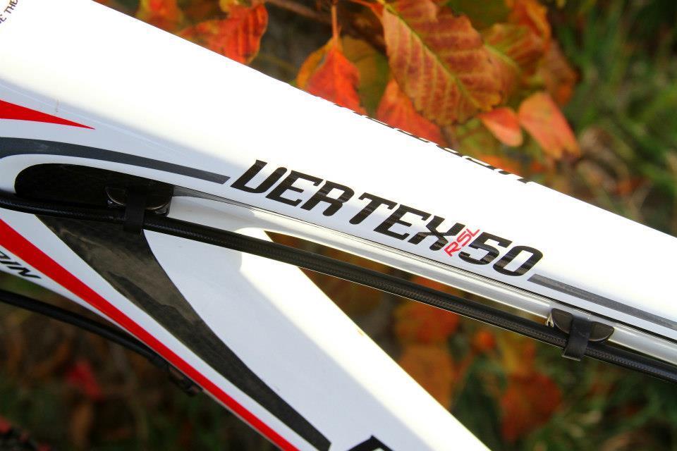 Rocky Mountain Vertex 50: Close-up of a white bike frame with the model name "VERTEX RSL 50" prominently displayed. The background features red and orange autumn leaves, suggesting an outdoor setting.