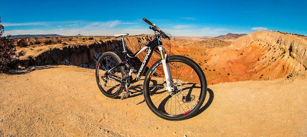 A black and white mountain bike resting on the edge of a desert cliff, with vibrant red rocks and a clear blue sky in the background. The landscape features rugged terrain and distant mountains, showcasing an adventurous outdoor setting. White Ridge Bike Trails mountain bike trail.