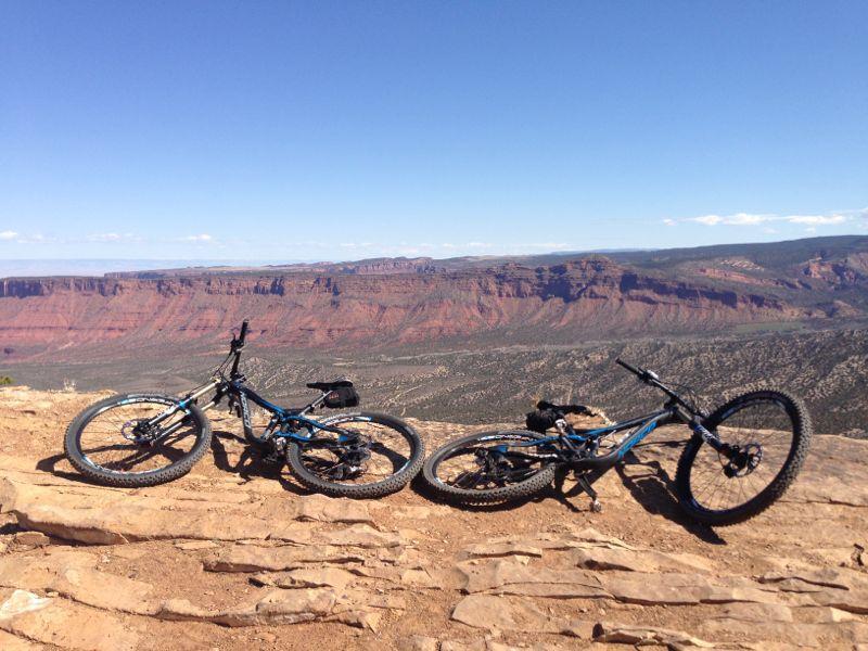 Two mountain bikes resting on rocky terrain overlooking a vast, scenic landscape with red rock formations under a clear blue sky. Porcupine Rim mountain bike trail.