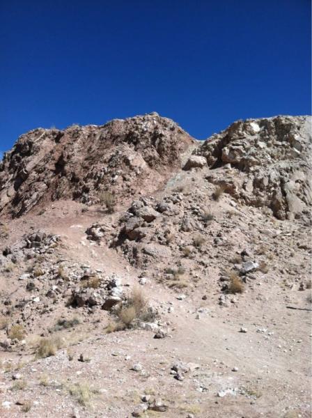 A rugged, rocky terrain under a clear blue sky, featuring steep, uneven slopes of reddish-brown and grayish rocks. Sparse vegetation is visible among the rocky surfaces, indicating a dry, arid environment. The image captures the natural landscape's stark beauty and geological characteristics. White Ridge Bike Trails mountain bike trail.