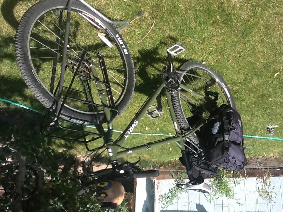 Surly Ogre: A green mountain bike is lying on its side on a grassy area, featuring a rear rack and a black backpack attached to the side.