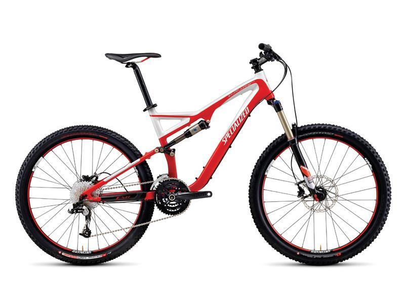 Specialized Stumpjumper FSR: A red and white mountain bike with a sleek design, featuring large knobby tires, a dual suspension system, and a Shimano drivetrain. The bike is positioned on a plain background, showcasing its modern frame and components.