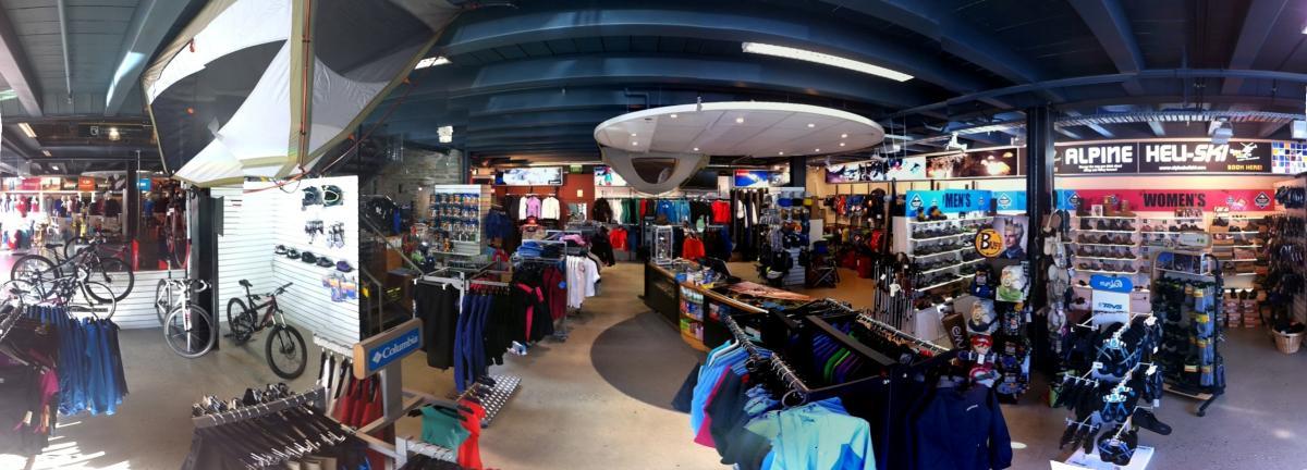 A panoramic view of an outdoor sports store showcasing a wide variety of equipment and apparel. The interior features clothing racks displaying men