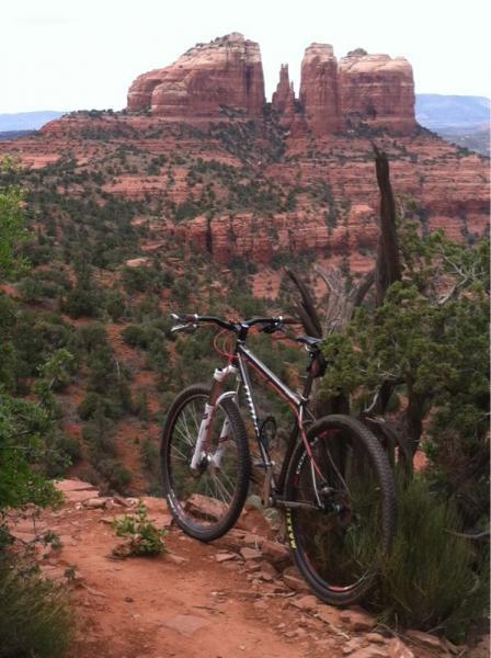 A mountain bike resting on a dirt path, overlooking a scenic view of red rock formations and distant mountains under a cloudy sky.  Hiline mountain bike trail.