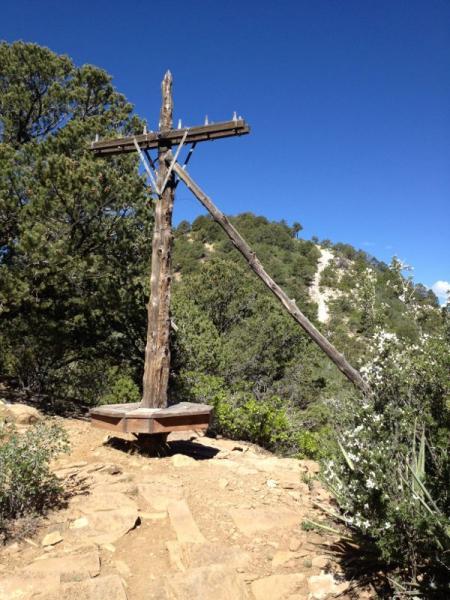 A wooden utility pole with crossbeams stands on a rocky path surrounded by greenery, under a clear blue sky. Horse Gulch mountain bike trail.