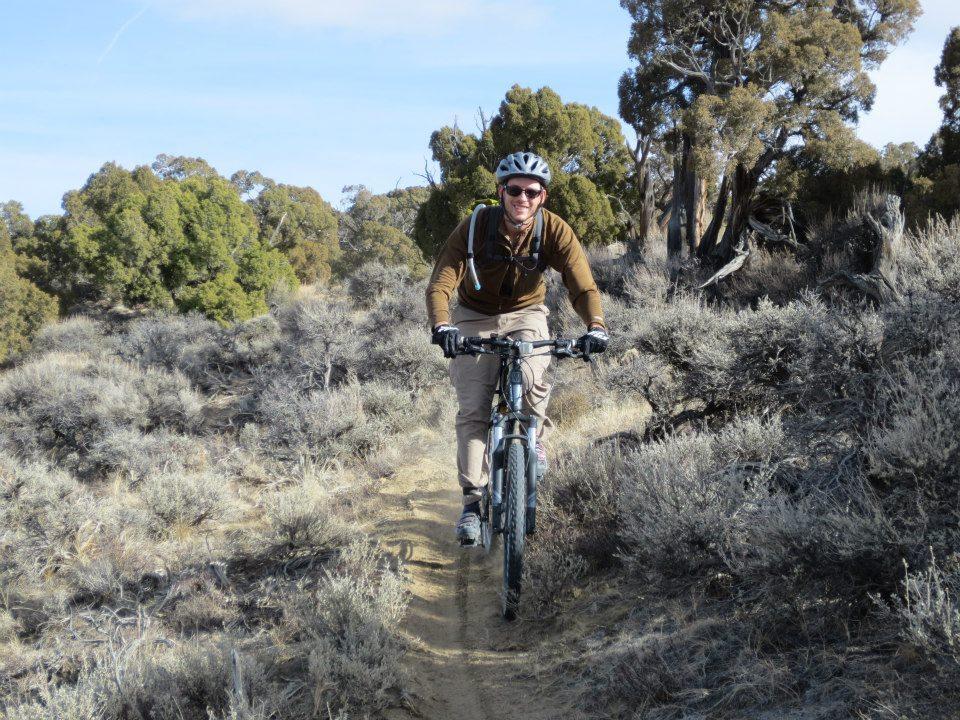 Trek 4500: Mountain biker riding on a dirt trail surrounded by sparse vegetation and trees on a sunny day. The rider is wearing a helmet and sunglasses, smiling while navigating the path.