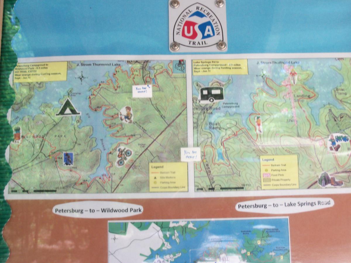 Map of J. Strom Thurmond Lake and surrounding areas, featuring recreation trails, camping sites, and points of interest. Includes routes from Petersburg to Wildwood Park and Lake Springs Road, with marked legends for parking areas, trails, and camping. Also contains notes for visitors on safety during hunting seasons. Bartram Trail / West Dam / Wildwood Park mountain bike trail.