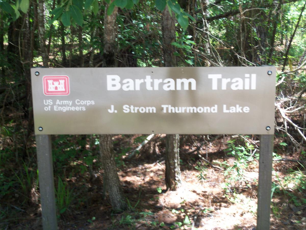 Sign for the Bartram Trail at J. Strom Thurmond Lake, displayed among greenery, indicating a path managed by the US Army Corps of Engineers. Bartram Trail / West Dam / Wildwood Park mountain bike trail.