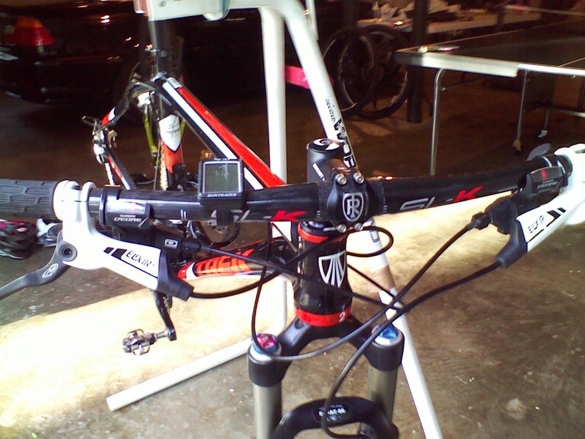 Trek Superfly 100 AL: Alt text: Close-up view of a mountain bike's handlebars, showcasing the grips, brake levers, and a display unit, with parts labeled and a partially visible bike frame in the background.