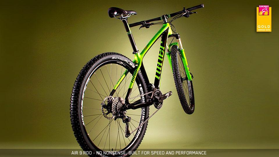 Niner Air 9 Carbon: A high-performance mountain bike with a striking green frame, featuring wide tires and a modern design. The bike is positioned against a dark green background, emphasizing its features, such as the gear system and suspension. Text at the bottom highlights its build quality and speed capabilities.