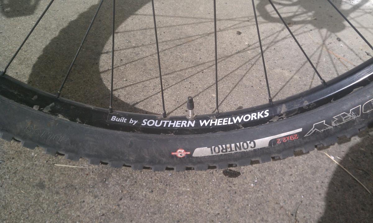 Specialized Stumpjumper FSR Comp 29: A close-up view of a bicycle wheel resting on a concrete surface. The wheel features a black rim with the text "Built by SOUTHERN WHEELWORKS" prominently displayed. The tire is labeled "CONTINENTAL" with additional specifications visible, indicating the size as 29x2.2. The image captures the spokes and valve stem of the wheel.