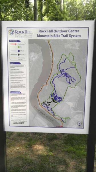 Map of the Rock Hill Outdoor Center Mountain Bike Trail System, displaying various trails in different colors, with a legend indicating trail types and difficulty levels. The layout shows the relationship between trails and surrounding features, such as a river, and includes information about safety and amenities. River walk mountain bike trail.