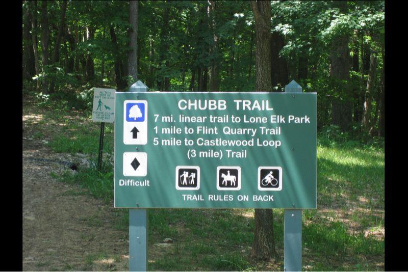 Sign for Chubb Trail, indicating a 7-mile linear trail to Lone Elk Park, 1 mile to Flint Quarry Trail, and 5 miles to Castlewood Loop (3-mile trail). The sign also notes that the trail is rated as difficult and includes icons for hiking, horseback riding, and biking. Chubb Trail mountain bike trail.