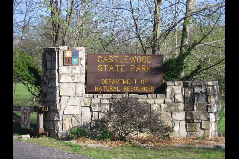 A wooden sign at the entrance of Castlewood State Park, featuring the name of the park and the Department of Natural Resources, surrounded by stone walls and greenery.  Castlewood State Park mountain bike trail.