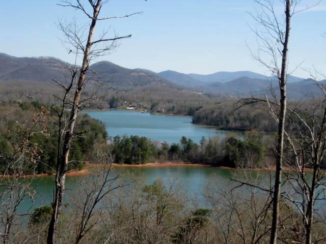 Scenic view of a tranquil lake surrounded by hills and mountains, with bare trees in the foreground and lush greenery along the water's edge. The landscape captures the serene beauty of nature on a clear day. Jack Rabbit Trails mountain bike trail.
