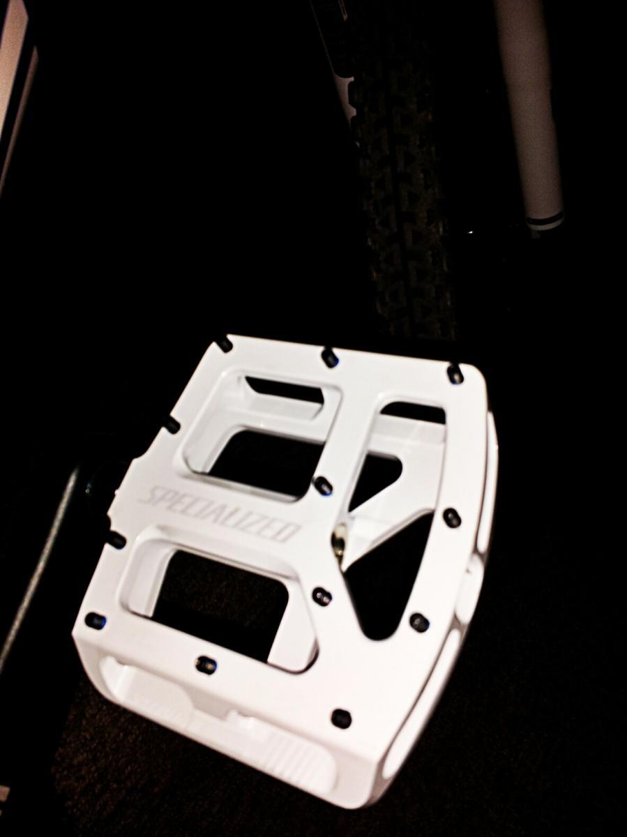 Felt Virtue Two: White bicycle pedal with a textured surface and bolt holes, positioned on a dark background. The pedal is part of a mountain bike setup.